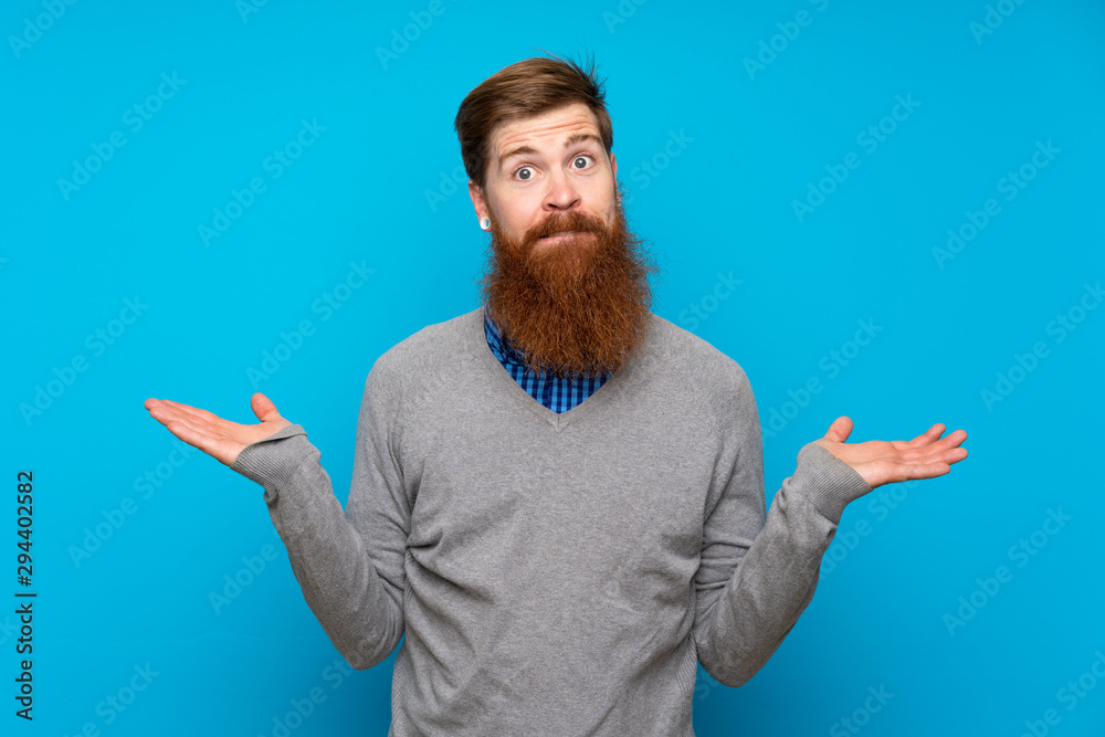 Redhead man with long beard over isolated blue background having doubts while raising hands