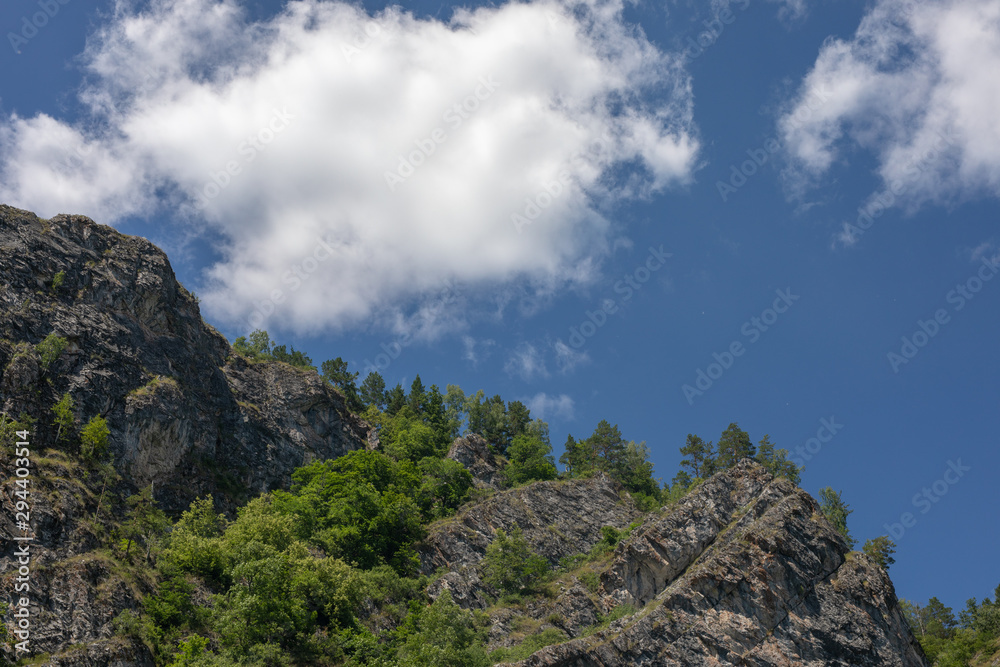 photograph of mountain peaks on clear sunny day. white clouds in blue sky on background.