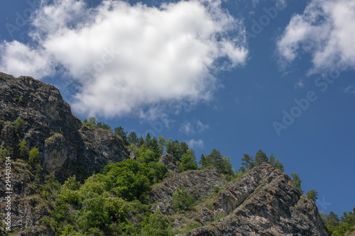 photograph of mountain peaks on clear sunny day. white clouds in blue sky on background.