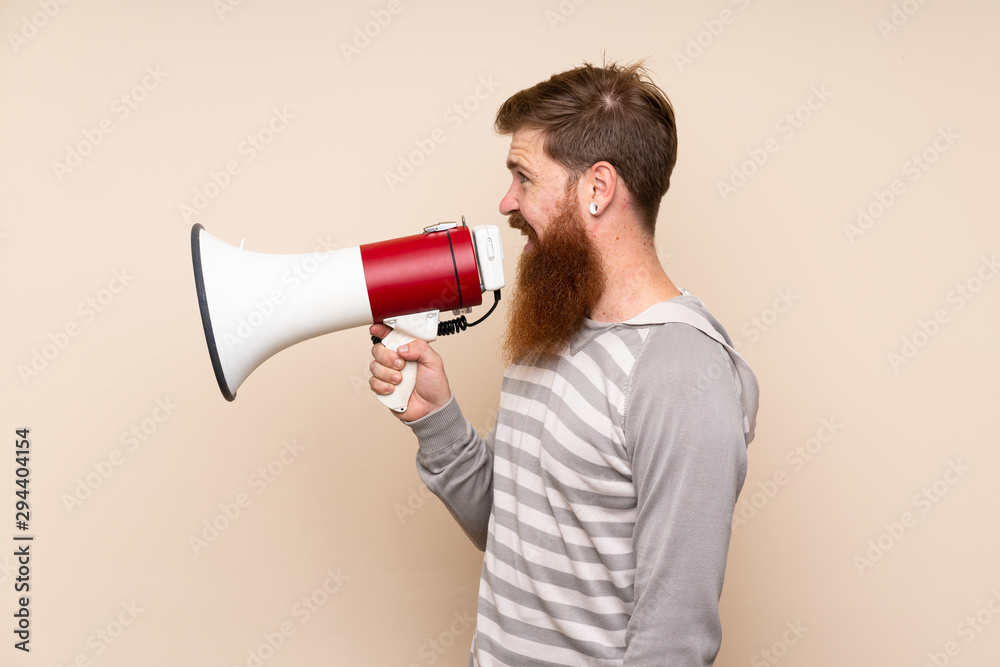 Redhead man with long beard over isolated background shouting through a megaphone Redhead man with long beard over isolated background shouting through a megaphone