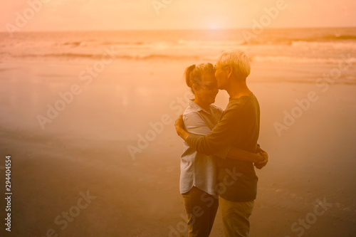 Senior lovers happily hug and kiss each other around the beach at sunset and soak up the atmosphere.