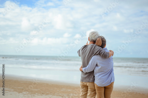 A senior couple hugged each other at the beach in the morning. The old man pointed the finger to the old woman to look at the bright blue sky, life insurance plan at the retirement concept. photo