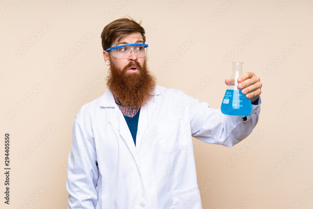 Redhead man with long beard over isolated background with a scientific test tube Redhead man with long beard over isolated background with a scientific test tube
