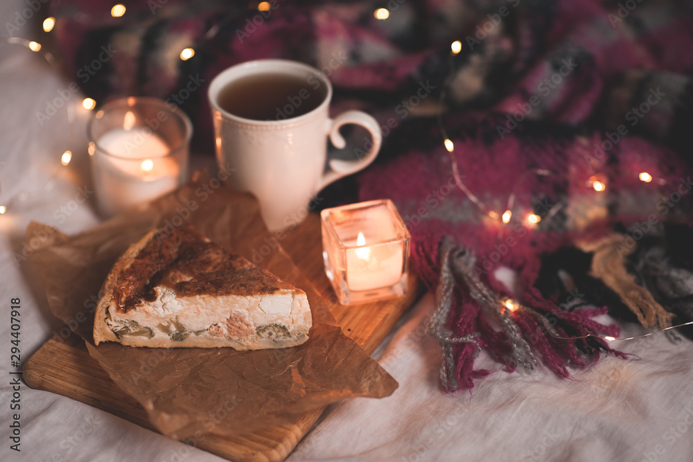 Winter pie with fresh cup of tea and burning candle in bed close up. Evening time.