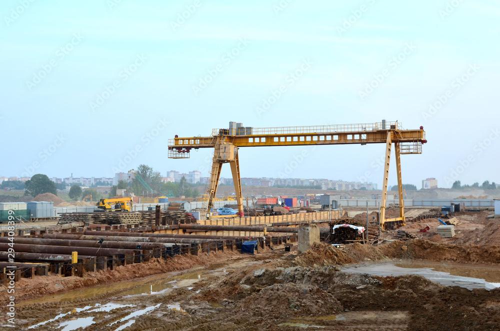 Yellow gantry bridge crane on the open area of subway construction project. Сut-and-cover construction Metro Station. Excavation pit of the 