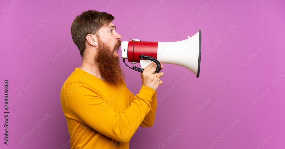 Redhead man with long beard over isolated purple background shouting through a megaphone Redhead man with long beard over isolated purple background shouting through a megaphone
