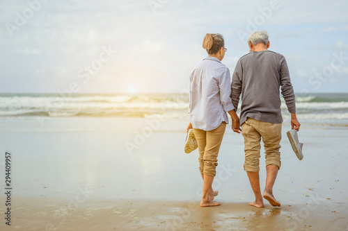 Senior couple walking on the beach holding hands at sunrise, plan life insurance at retirement concept. photo