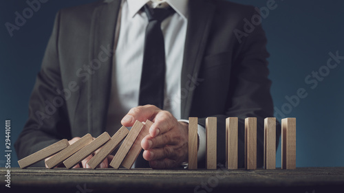 Business executive stopping collapsing dominos with his hand photo