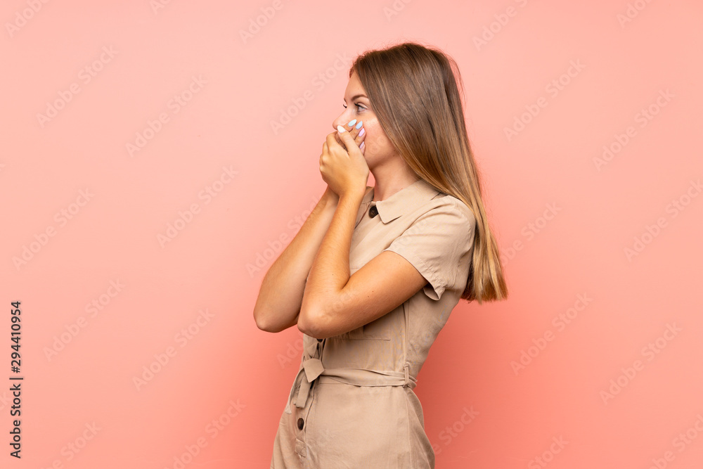 Lithuanian blonde girl over isolated pink background covering mouth and looking to the side Lithuanian blonde girl over isolated pink background covering mouth and looking to the side