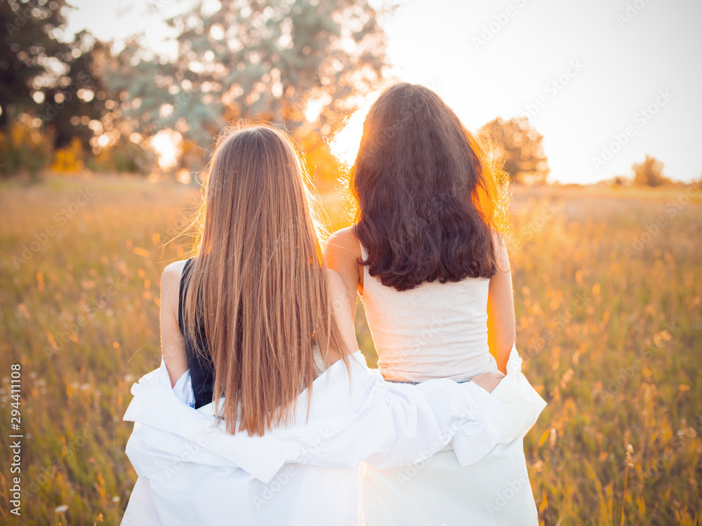 Two girls in white shirts looking on the sunset. Best friends - obrazy, fototapety, plakaty 