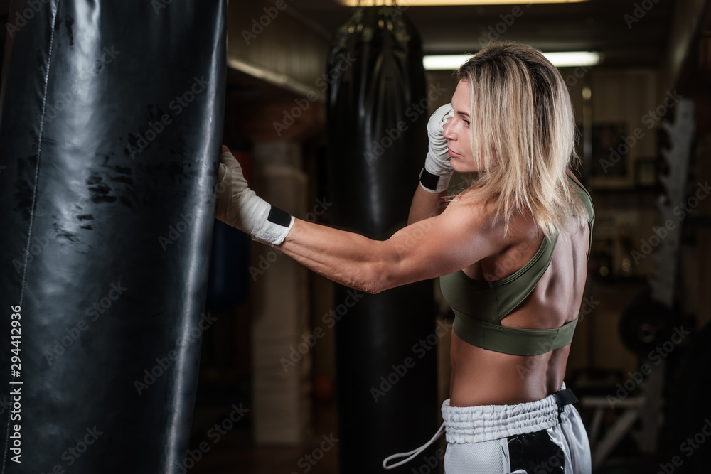 Attractive blond woman has a boxing training with punching bag at kick boxing studio.