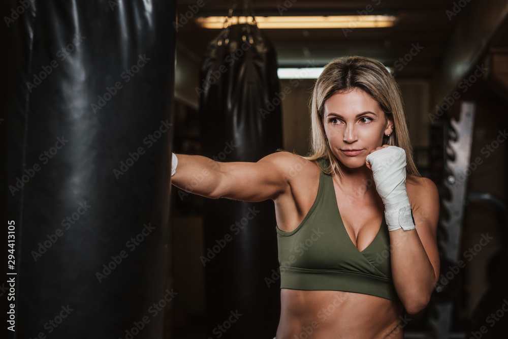 Muscular pretty woman is doing her kickboxing exercises with punching bag.