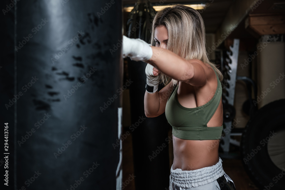 Beautiful boxer female has her training with punching bag at gym.