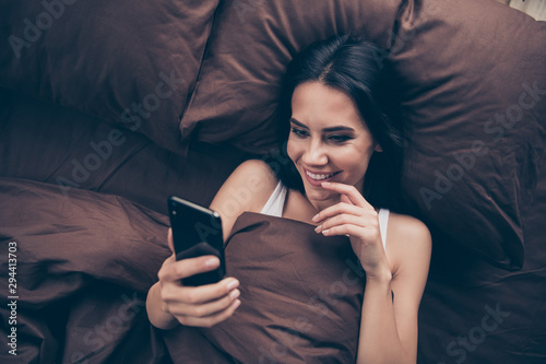 Top above high angle view close-up portrait of her she nice attractive lovely flirt charming cute cheerful cheery girl using gadget sending photos lying in bed in room flat house indoors