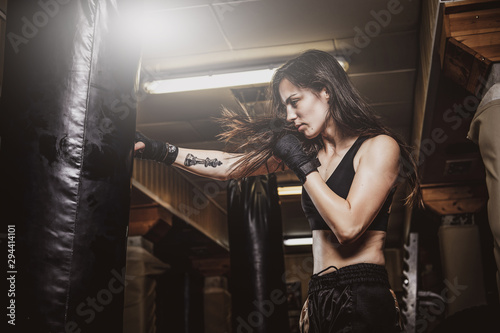 Skinny focused woman has a boxing training with punching bag at dark gym. © Fxquadro