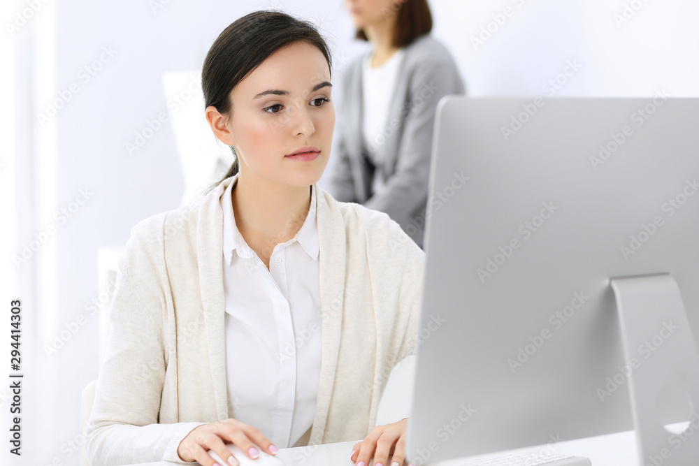 Business woman working with computer in office, female colleague at background. Headshot of Lawyer or accountant at work while sitting at the desk Business woman working with computer in office, female colleague at background. Headshot of Lawyer or accountant at work while sitting at the desk