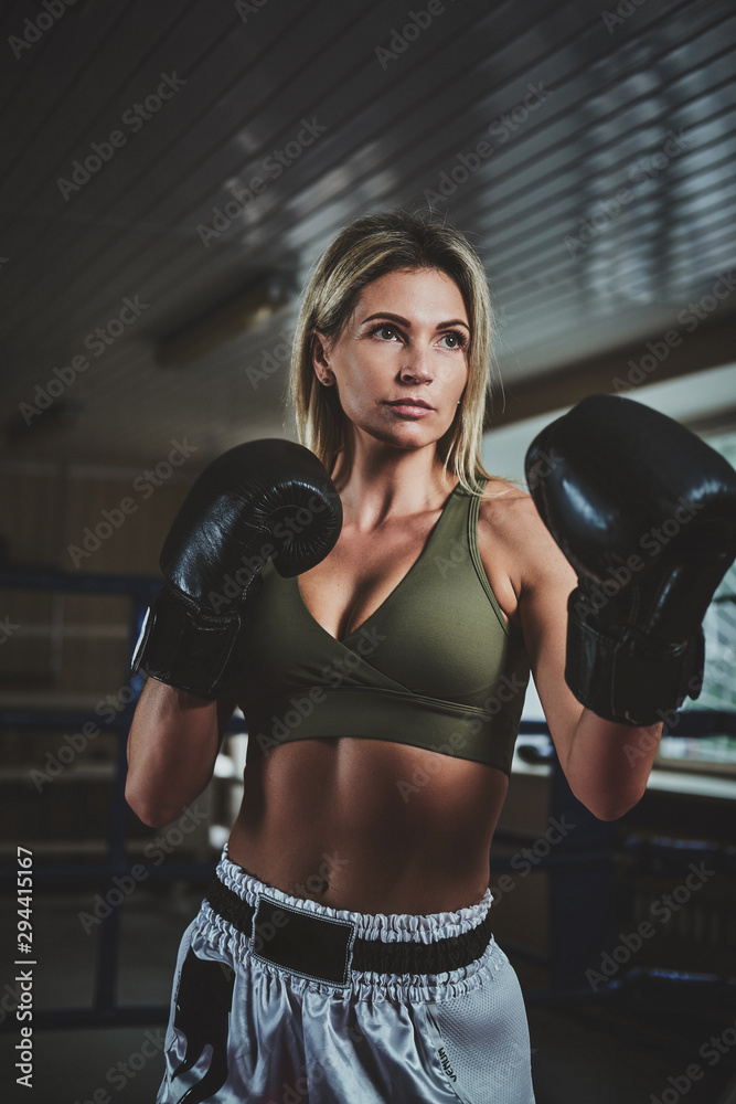 Beautiful female boxer is posing for photographer wearing boxing gloves.