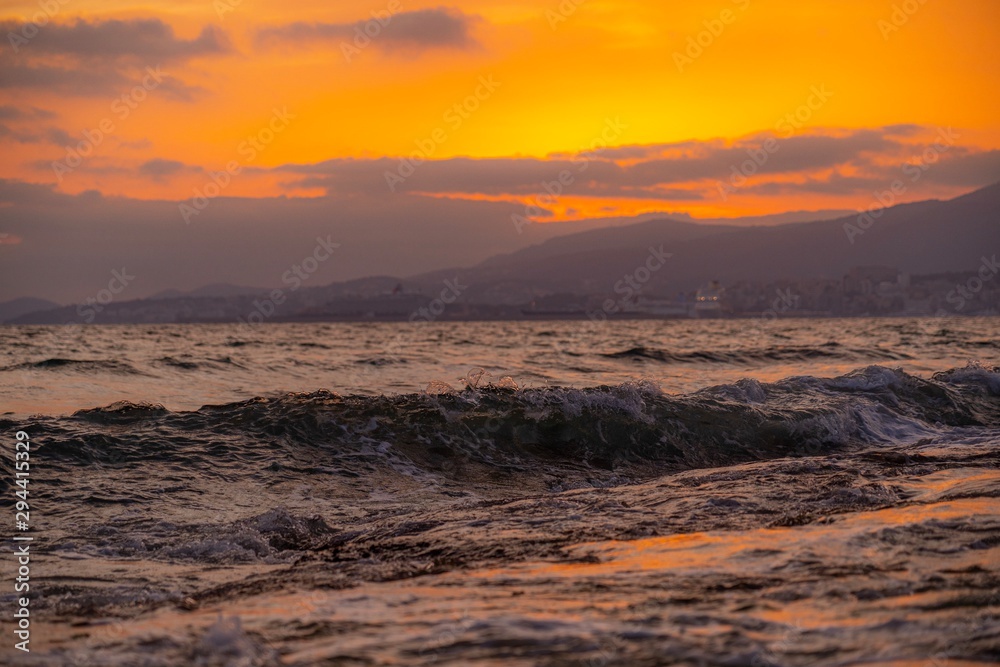 Gold glowing wave breaking on the rocks at sunset with reflections on the rocks