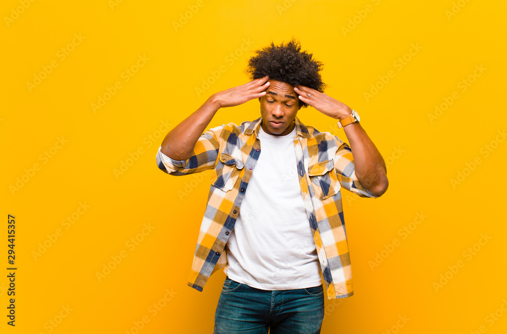 young black man looking concentrated, thoughtful and inspired, brainstorming and imagining with hands on forehead against orange wall - obrazy, fototapety, plakaty 