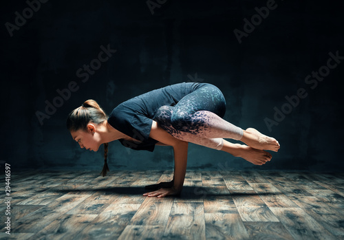 Young attractive woman practicing yoga doing side crane pose in dark room photo