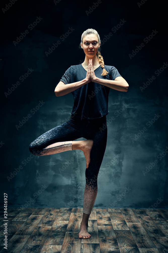 Young beautiful woman doing yoga asana Tree Pose in dark room