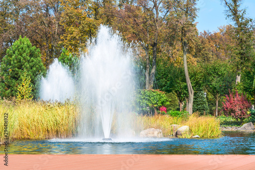  Fragment of the park in Mezhyhiria near Kiev, fountains on the lake. Scenery of nature with sunlight.