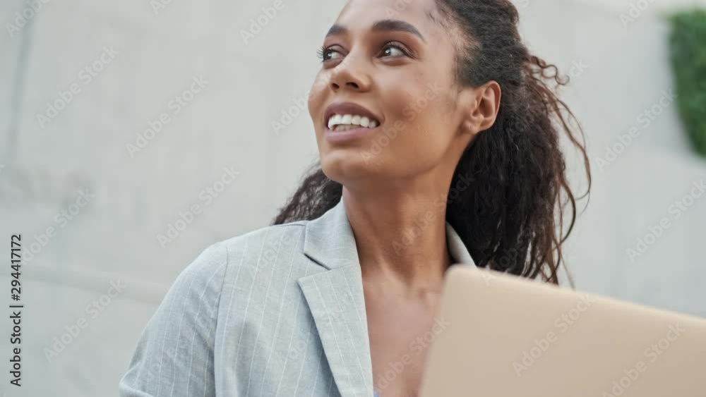 Close up view of beautiful young african business woman working on laptop while sitting outdoors at the stairs Close up view of beautiful young african business woman working on laptop while sitting outdoors at the stairs