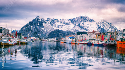 Fishing boats at harbour of cozy small fishing village Henningsvaer in Lofoten Islands, Northern Norway. Amazing landscape with mountains and reflection in the water, travel winter background