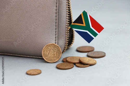 Heap of South African Rand coin money and mini South African flag stick on the leather wallet on grey background.