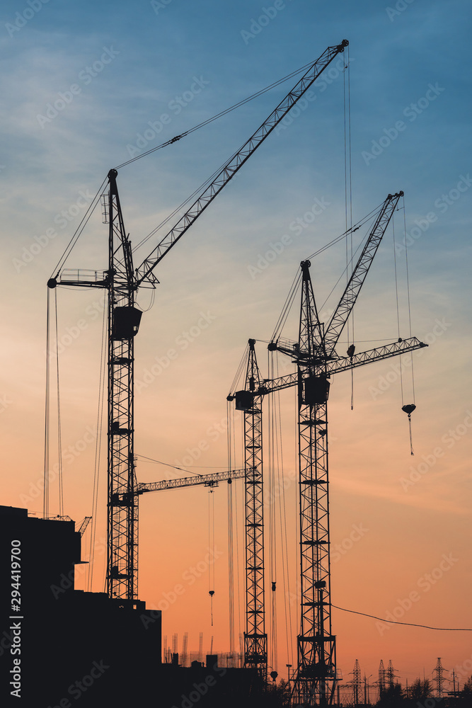 silhouettes of construction cranes at sunset