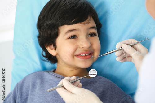 Little arab boy sitting at dental chair with open mouth during oral check up while doctor. Visiting dentist office. Medicine and stomatology concept