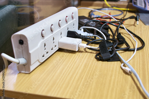 Many electrical wires plug into electric power bar on the table.