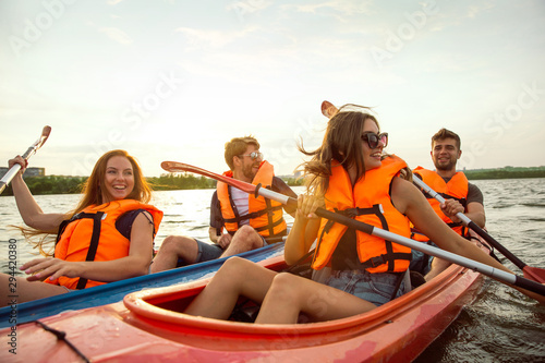 Happy young caucasian group of friends kayaking on river with sunset in the backgrounds. Having fun in leisure activity. Happy male and female model laughting on the kayak. Sport, relations concept. © master1305
