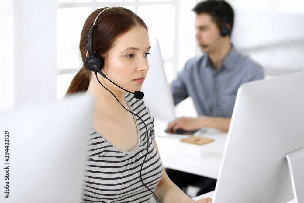 Group of operators at work. Call center. Focus on beautiful woman receptionist in headset at customer service. Business concept and casual striped clothing style Group of operators at work. Call center. Focus on beautiful woman receptionist in headset at customer service. Business concept and casual striped clothing style