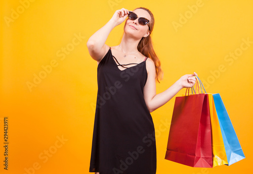 Cheerful and shopaholic young woman in studio over yellow background