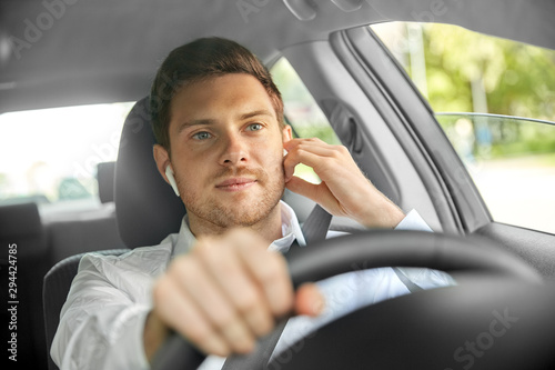transport, vehicle and people concept - man or driver with wireless earphones or hands free device driving car
