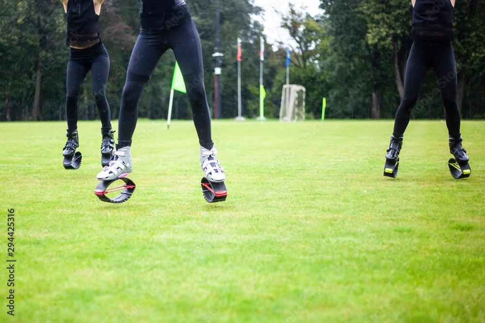 Girls in boots for jumping. Bouncing shoes on the legs of women. Sports performance on the football field in the rain. A new sport is jumping in special shoes on springs.