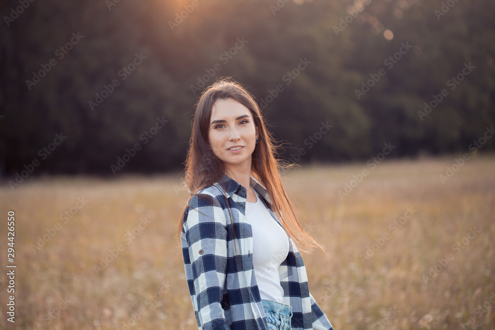 Beautiful girl in plaid shirt walking outdoors at sunset.