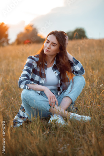 Beautiful young woman sitting on the grass at sunset. Eyes closed.