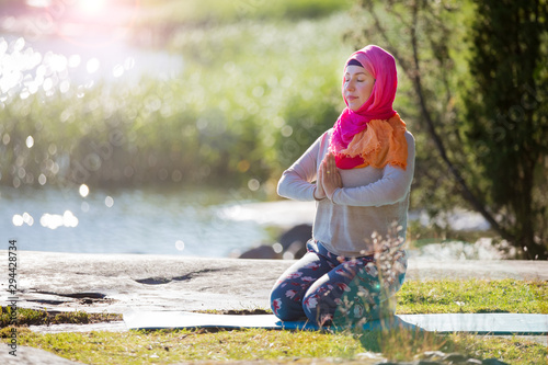 Fototapeta Naklejka Na Ścianę i Meble -  Attractive woman in hijab training in the park, meditating. Doing yoga exercises on fresh air and enjoying early morning. Healthy lifestyle