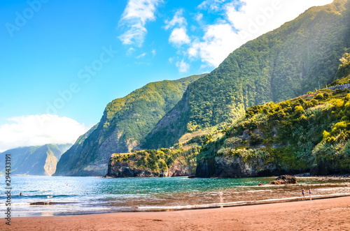 Beautiful sandy beach in Seixal, Madeira Island, Portugal. Green hills covered by tropical forest in the background. People on the beach. Summer vacation destination. Portuguese landscape