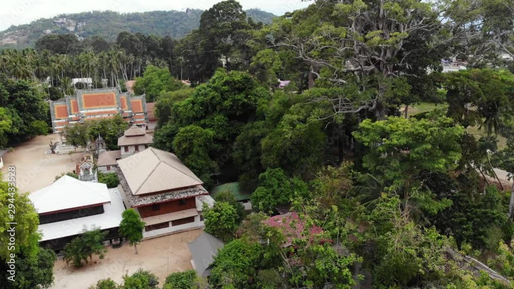 Classic Buddhist temple between forest. From above drone view classic Buddhist monastery between green trees near hill in Thailand. Koh Samui. concept of tourism, meditation and oriental life. Classic Buddhist temple between forest. From above drone view classic Buddhist monastery between green trees near hill in Thailand. Koh Samui. concept of tourism, meditation and oriental life.