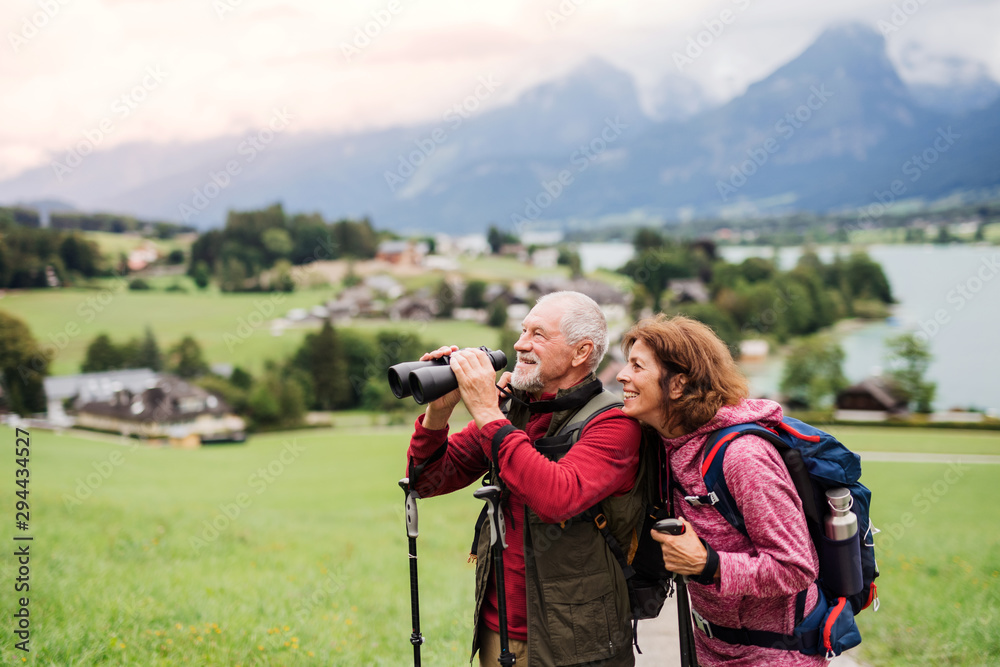 Senior pensioner couple with hiking in nature, using binoculars.