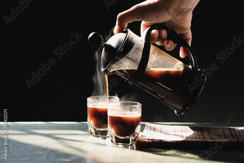 Aromatic coffees with hot smoke are poured into couple cup from French press coffee maker, Hot drink is good for health,On old wood table,Black background,Natural light,Selective focus,Vintage style. photo