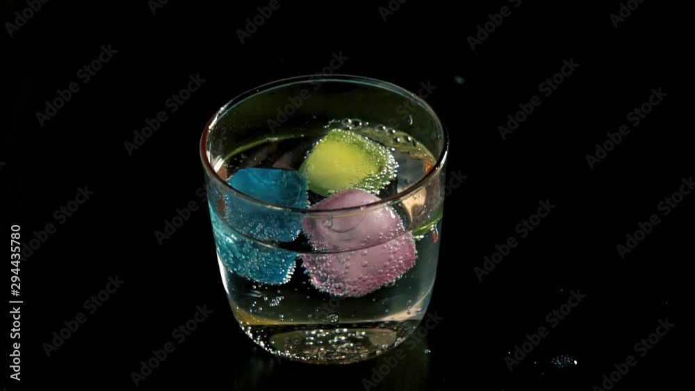 Colorful plastic ice cubes are turning in a glass of soda in slow motion
