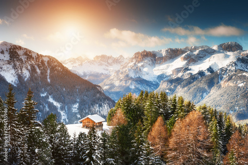 Wooden house in winter mountains at sunset. Ski resort in Dolomite Alps. Val Di Fassa, Italy. Beautiful winter landscape
