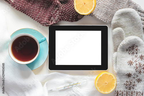 Digital tablet with blank screen with copy space, cup of hot tea, lemon and hand with thermometer on a white table background. photo