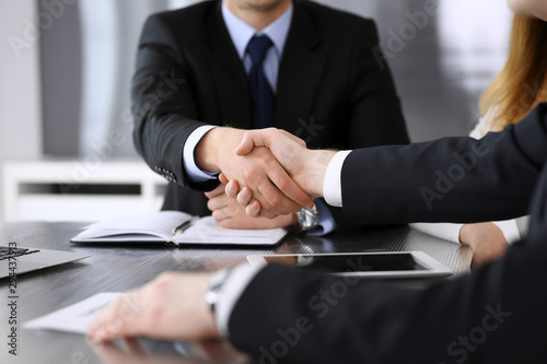 Businessman shaking hands with his colleague or partner above the glass desk in modern office, close-up. Unknown business people at meeting. Teamwork, partnership and handshake concept