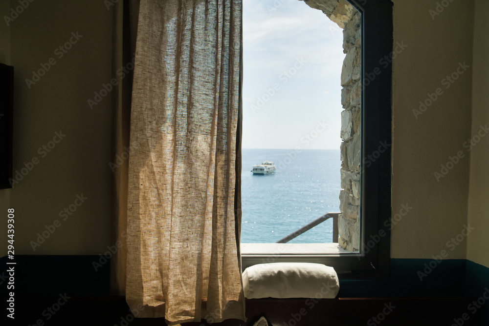 Window view of a room on the sea, a sailing boat in the distance, Cinque Terre, Italy