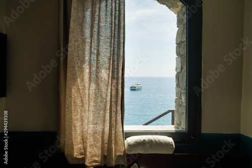 Window view of a room on the sea, a sailing boat in the distance, Cinque Terre, Italy